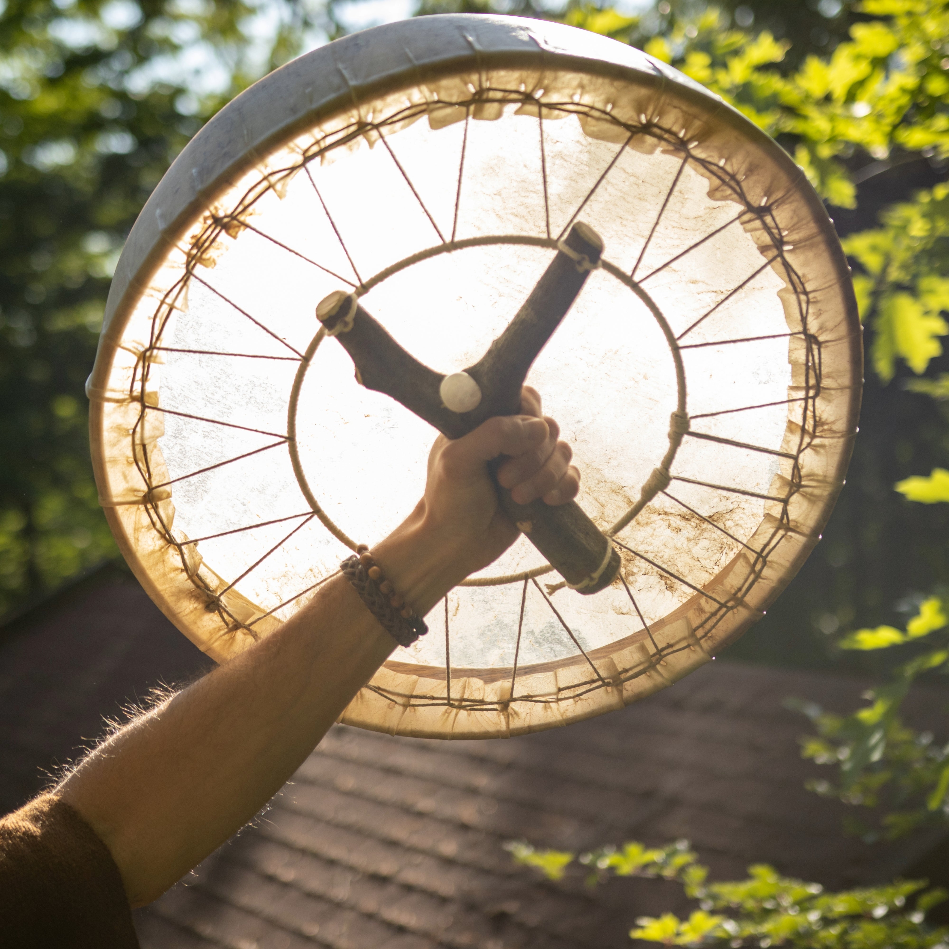 Eine schamanische Rahmentrommel mit Bergkristall wird in der Hand gehalten. Buchenholzrahmen und Rinderfell mit einer Astgabel aufgespannt.